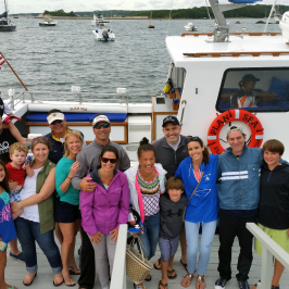 group of people different ages posing on dock with boat in the back