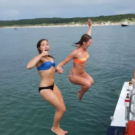 two girls jumping off the side of the boat into the water