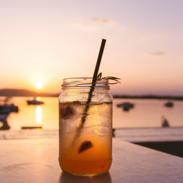 glass with an iced drink in the foreground, sunset in the background